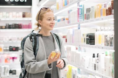 Sarışın genç kadın seyahat seyahat etmek sırt çantası Havaalanı duty free mağazasında parfüm seçimi giyiyor.