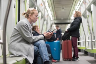 Telefonda metro toplu taşıma araçları ile seyahat ederken okuma kış ceket giyen güzel sarışın kadın.