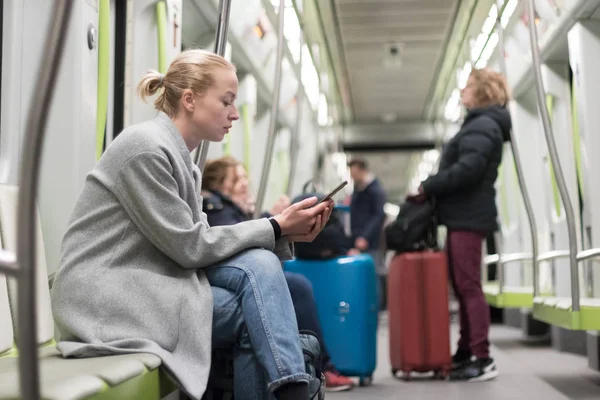 Mooie blonde vrouw draagt winterjas lezen op de telefoon terwijl het reizen met de metro openbaar vervoer. — Stockfoto