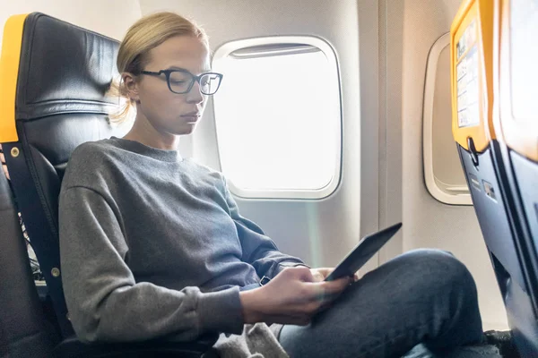 Kobieta nosi okulary czytanie na e czytnik, cyfrowych podczas podróży samolotem. — Zdjęcie stockowe