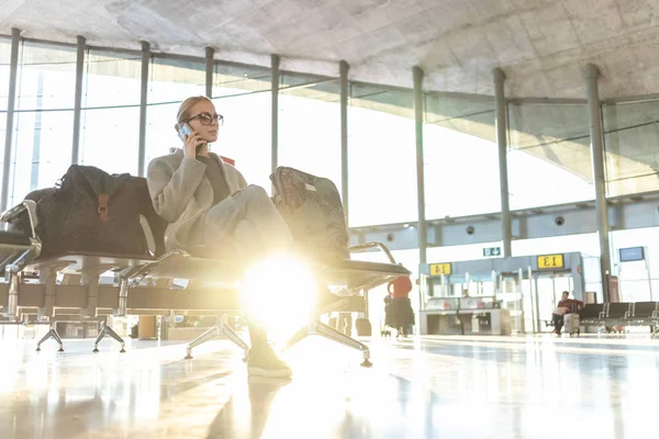 Žena cestujícím mluvit na její mobil při čekání na palubu letadla u odletových bran na letišti v terminálu. — Stock fotografie