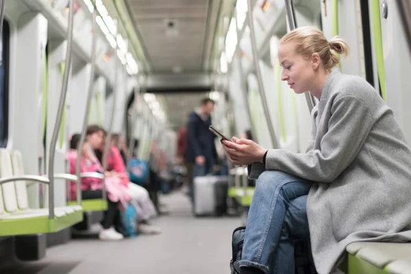 Telefonda metro toplu taşıma araçları ile seyahat ederken okuma kış ceket giyen güzel sarışın kadın. — Stok fotoğraf