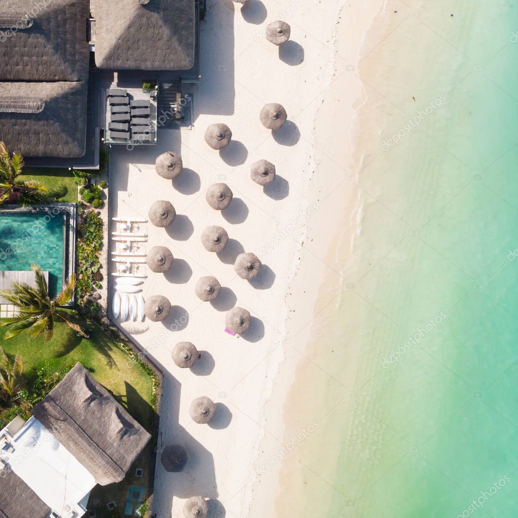 Aerial view of amazing tropical white sandy beach with palm leaves umbrellas and turquoise sea, Mauritius.