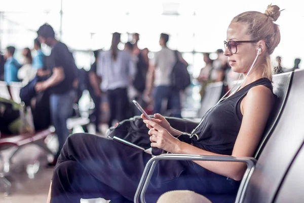 Kvinnlig resenär som använder sin mobiltelefon medan hon väntar på att gå ombord på ett plan vid avgångsporten vid asiatiska flygplatsterminalen. — Stockfoto