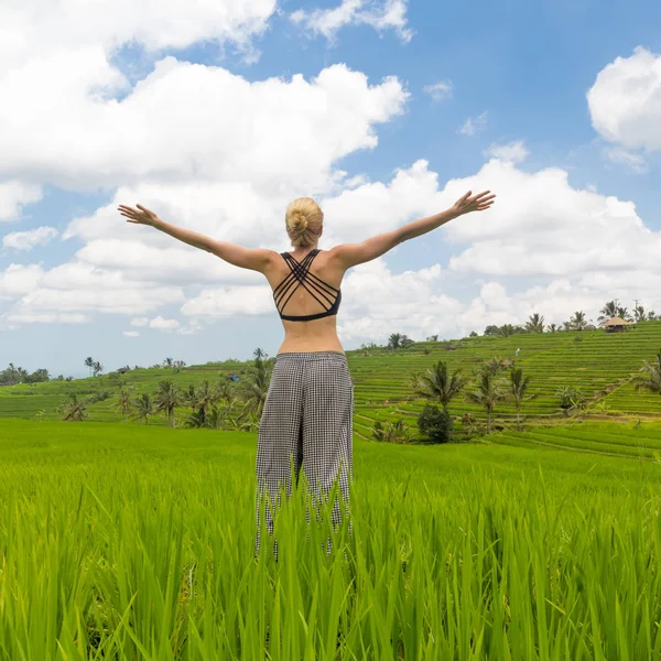 Entspannte, lässig-sportliche Frau, die Arme in den Himmel gereckt, genießt die reine Natur der wunderschönen grünen Reisfelder auf Bali. — Stockfoto