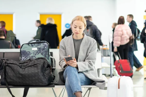 Viajero femenino usando su teléfono celular mientras espera para abordar un avión a las puertas de salida en la terminal del aeropuerto . — Foto de Stock