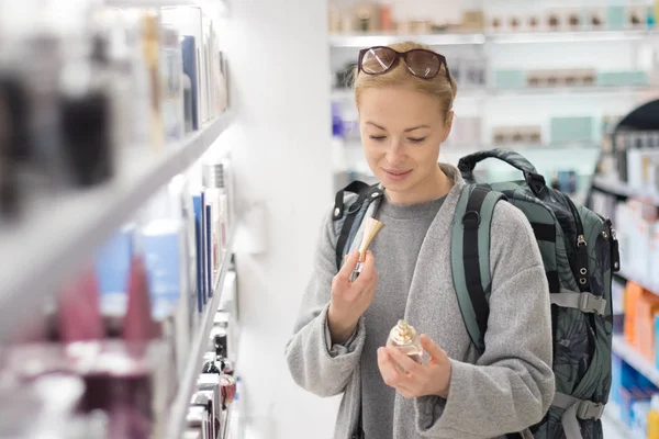 Блондинка молода жінка мандрівник в рюкзаку подорожі вибираючи парфуми в магазині безмитної торгівлі аеропорту . — стокове фото