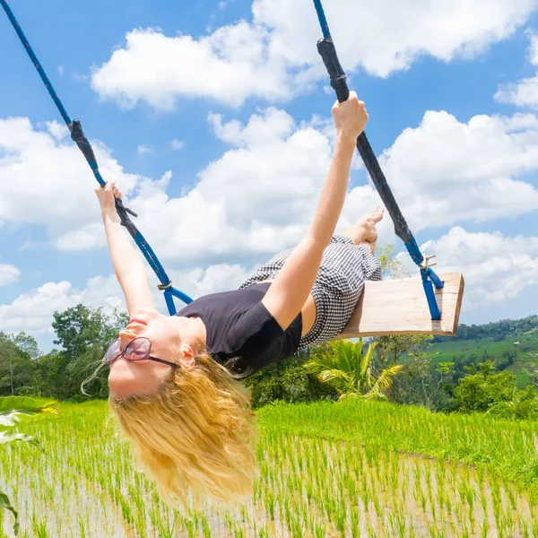 Felice viaggiatore femminile oscillante su altalena di legno, godendo di vacanza estiva tra terrazze di riso verde incontaminato . — Foto Stock