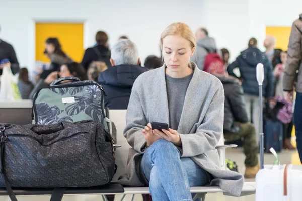 Reisende benutzt ihr Handy, während sie am Abflugsteig des Flughafenterminals auf ein Flugzeug wartet. — Stockfoto