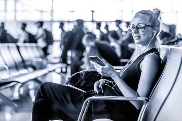 Женщина-путешественница использует свой мобильный телефон в ожидании посадки на самолет у вылета в азиатском терминале аэропорта. Синий тонированный черно-белый снимок . — стоковое фото