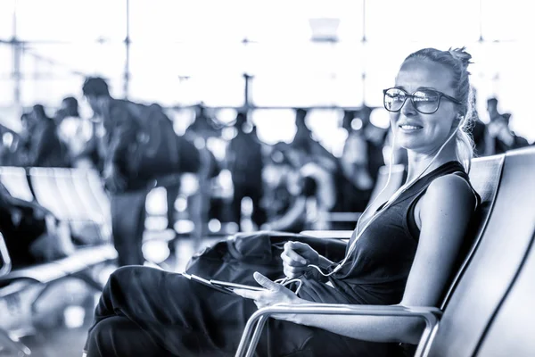 女性旅行者在亚洲机场航站楼登机口等候登机时使用手机。蓝色色调的黑白照片. — 图库照片