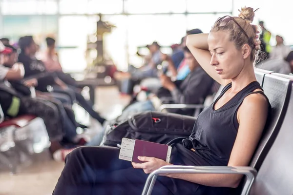 Alkalmi cserzett szőke női utas gazdaság mobiltelefon, útlevél- és beszállókártyáját, miközben arra vár, hogy fedélzetén a repülőgép a ázsiai reptéri terminálnál indulási kapu — Stock Fotó