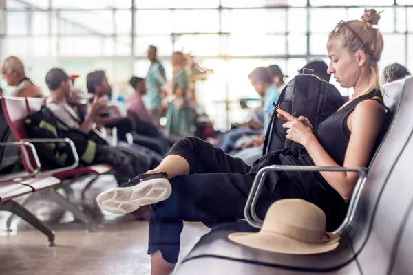 Kvinnlig resenär som använder sin mobiltelefon medan hon väntar på att gå ombord på ett plan vid avgångsporten vid asiatiska flygplatsterminalen. — Stockfoto