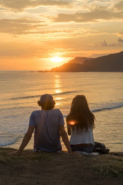 Ρομαντικό ζευγάρι στις διακοπές καθισμένος και βλέποντας το πολύχρωμο ηλιοβασίλεμα που απλώνεται πάνω από την ακτή της θάλασσας. — Φωτογραφία Αρχείου