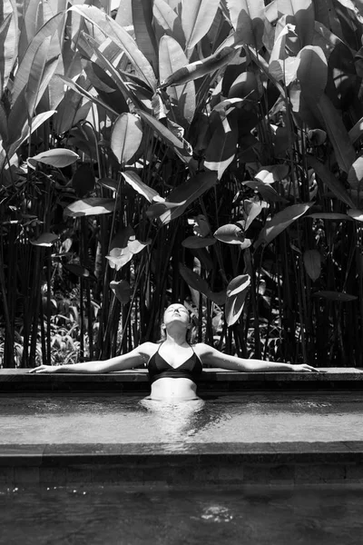 Sensuell ung kvinna koppla av i utomhus Spa infinity pool omgiven av frodig tropisk grönska i Ubud, Bali. Svartvit bild. — Stockfoto