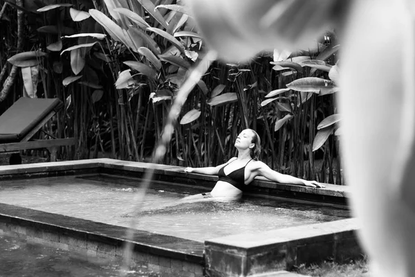 Sensuelle jeune femme se relaxant dans la piscine à débordement spa extérieur entouré de verdure tropicale luxuriante d'Ubud, Bali. Image en noir et blanc . — Photo