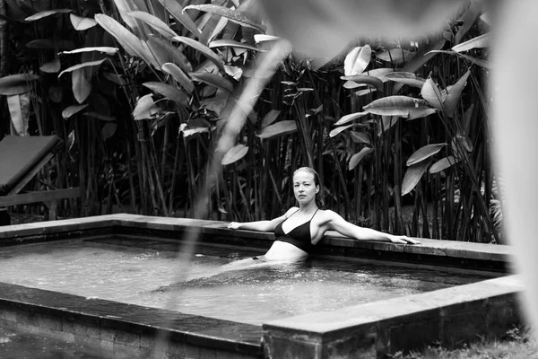 Sensual jovem mulher relaxante no spa ao ar livre piscina infinita cercada com vegetação tropical exuberante de Ubud, Bali. Imagem em preto e branco . — Fotografia de Stock