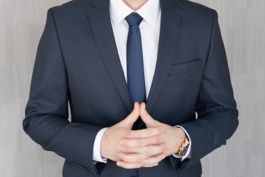 Torso of anonymous businessman standing with hands in lowered steeple, wearing beautiful fashionable classic navy blue suit. clipart
