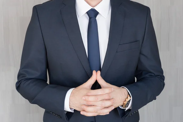 Torso of anonymous businessman standing with hands in lowered steeple, wearing beautiful fashionable classic navy blue suit. — Stock Photo, Image