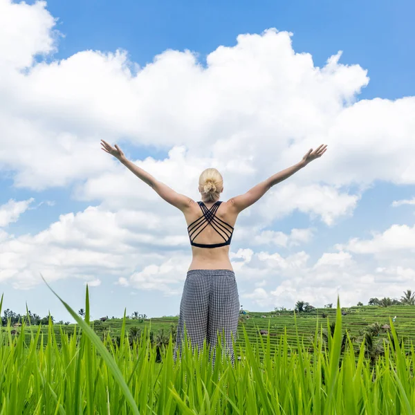 Relaxado mulher desportiva saudável, braços erguidos para o céu, desfrutando de natureza pura em belos campos de arroz verde em Bali . — Fotografia de Stock