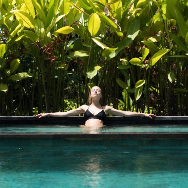 Dışardaki kaplıcada dinlenen şehvetli genç bir kadın sonsuz yüzme havuzunda çevresi yemyeşil Ubud, Bali ile çevrili..