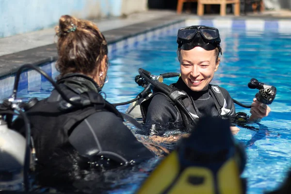 Woman getting first experience with scuba diving under the guidance of experienced recreational diving instructor in swimming pool.