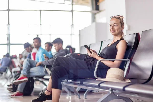 Kvinnlig resenär som använder sin mobiltelefon medan hon väntar på att gå ombord på ett plan vid avgångsporten vid asiatiska flygplatsterminalen. — Stockfoto