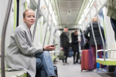 Güzel sarışın kadın metroyla seyahat ederken akıllı telefon kullanıyor..