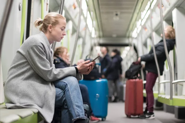 Mulher loira bonita vestindo casaco de inverno lendo no telefone enquanto viaja de metro transporte público . — Fotografia de Stock