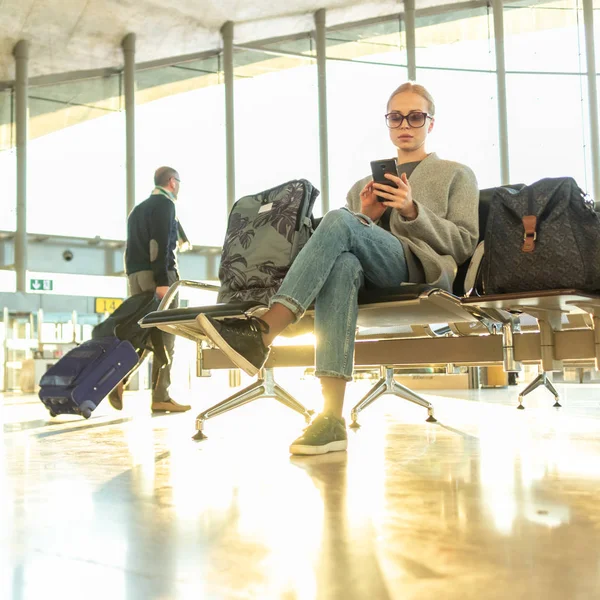 Женщина-путешественница использует свой мобильный телефон в ожидании посадки на самолет на выходе из терминала аэропорта . — стоковое фото