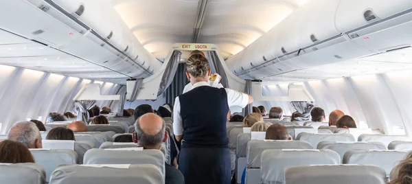 Interiör i kommersiella flygplan med flygvärdinna som betjänar passagerare på sittplatser under flygning. — Stockfoto