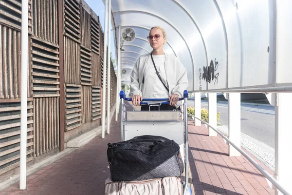 Молодая женщина перевозит багаж с парковки прибытия в международный аэропорт Термейнал на багажной тележке . — стоковое фото