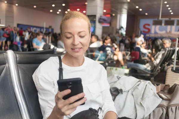 Mujer viajera leyendo en su teléfono celular mientras espera para abordar un avión a las puertas de salida en la terminal del aeropuerto . —  Fotos de Stock