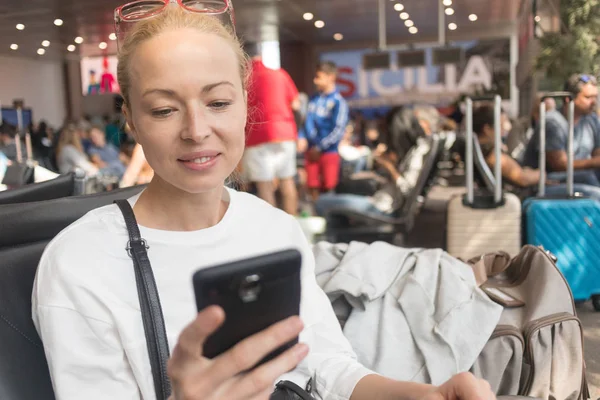 Mujer viajera leyendo en su teléfono celular mientras espera para abordar un avión a las puertas de salida en la terminal del aeropuerto . —  Fotos de Stock