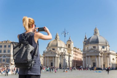 Kadın turist bir fashinable vintage hipster sırt çantası alarak fotoğraf ile Piazza del Popolo Roma, İtalya tarafından cep telefonu.