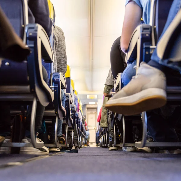 Low agle view of passenegers commercial airplane aisle with passenegers sitting on their seats while flying — Stock Photo, Image