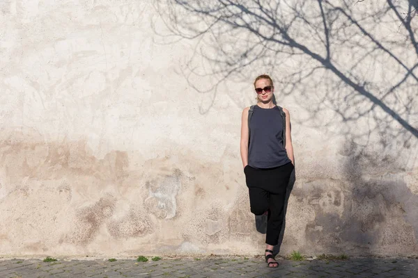 Grafisk och strukturerad artisic bild av moderna trendiga fashionabla kvinna bär solglasögon lutar mot gamla texturerat retro vägg med träd skugga faller på väggen. — Stockfoto