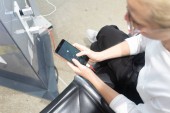 Mladá žena, která sedí u nabíjecí stanice a dívá se na svůj telefon. Dobíjení mobilních telefonů z bezplatné stanice na letišti.