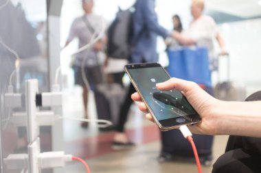 Elektrikli fiş ve şarj kablosu kullanarak halka açık bir yerde şarj ederken akıllı telefonu tutan ve kullanan kadın elleri