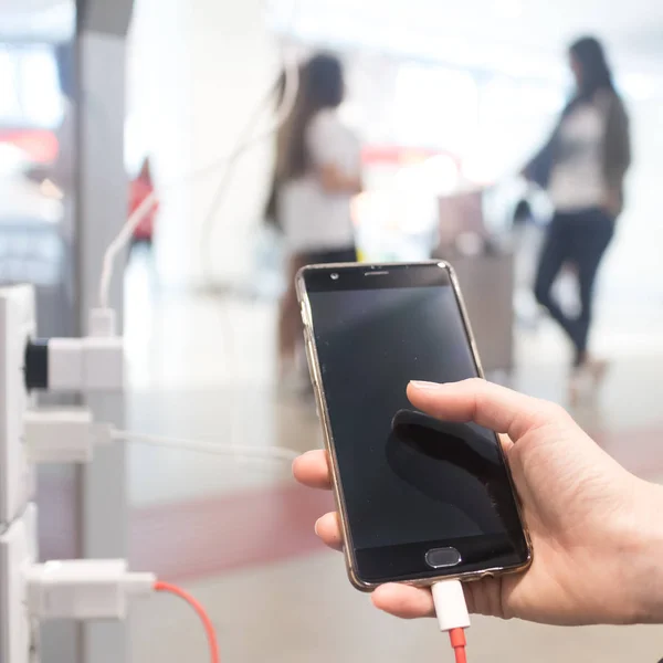 Manos femeninas sosteniendo y usando un teléfono inteligente mientras lo carga en un lugar público usando un enchufe eléctrico y un cable de carga — Foto de Stock