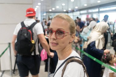 Genç bayan gezgin kalkış havaalanı terminalinde güvenlik kontrolünde uzun kuyrukta bekliyor. Bayan uçağa binmeden önce havaalanında kuyrukta bekliyor..