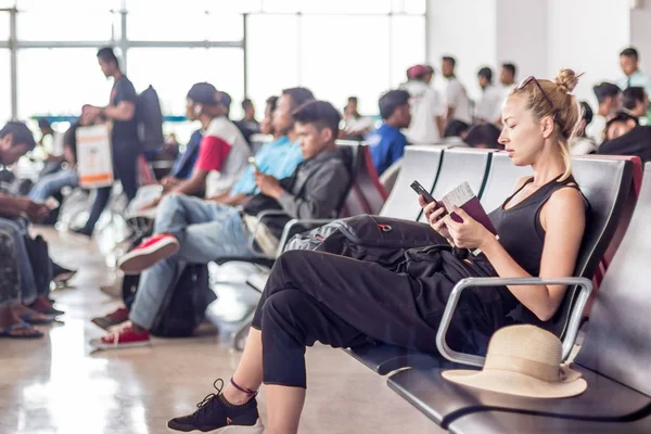 Жінка-мандрівник, яка використовує свій мобільний телефон, чекає на літак біля воріт вильоту в терміналі азіатського аеропорту . — стокове фото