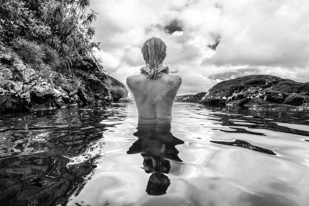 Naked woman bathing and relaxing in natural swimming pool in black and white.