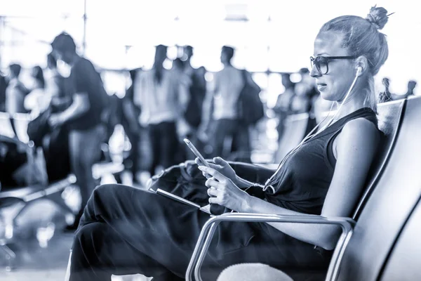 Női utas használ őt sejt telefon várva, hogy fedélzetén a repülőgép indulási kapuk ázsiai reptéren. Kék tónusú fekete-fehér fénykép. — Stock Fotó