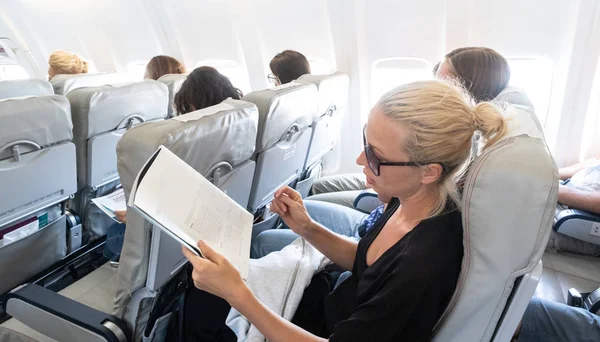 Egy nő magazint olvas repülőn repülés közben. Női utazó olvasás ülő utas kabin. — Stock Fotó