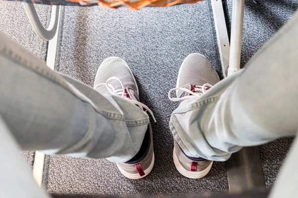 Penumpang pria dengan jarak kaki yang sedikit pada penerbangan pesawat komersial yang panjang. Fokus pada sepatu olahraga kasual — Stok Foto