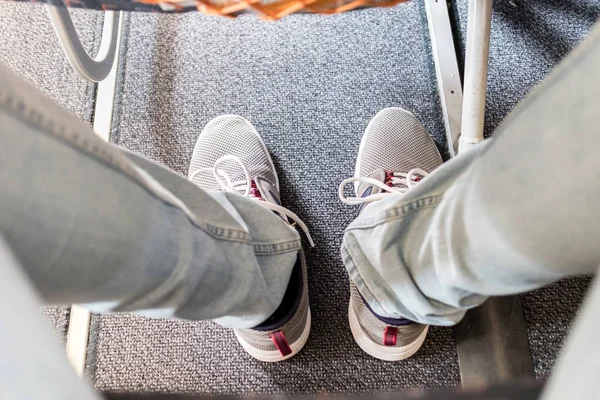 Manlig passagerare med brist på benutrymme på långa kommersiella flygplan flygning. Fokus på casual sportiga sneakers — Stockfoto