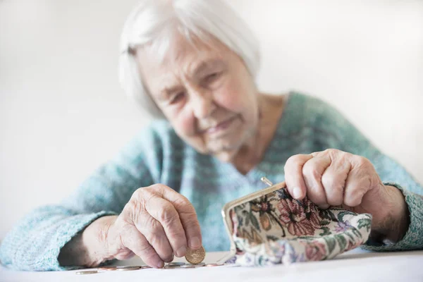 Besorgte ältere Frau sitzt am Tisch und zählt Geld im Portemonnaie. — Stockfoto