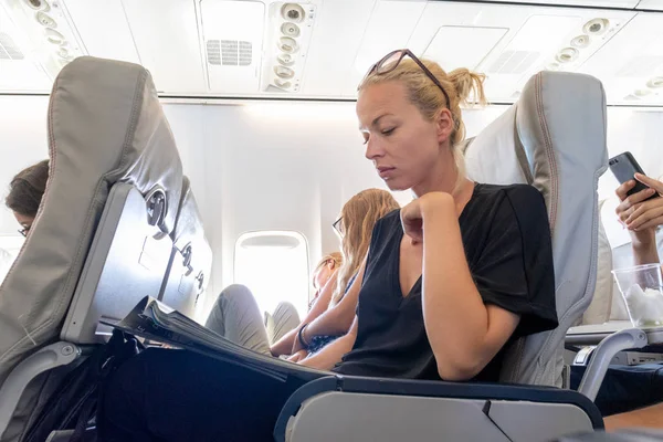 Женщина читает журнал в самолете во время полета. Женщина-путешественница, сидящая в пассажирской каюте . — стоковое фото