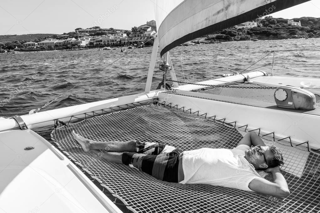 Sporty man relaxing on a luxury catamaran sailing boat.